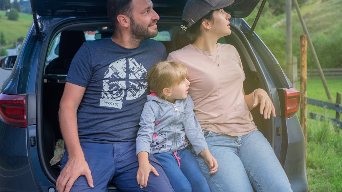 A family sits in a car trunk, enjoying an outdoor adventure in a scenic countryside.
